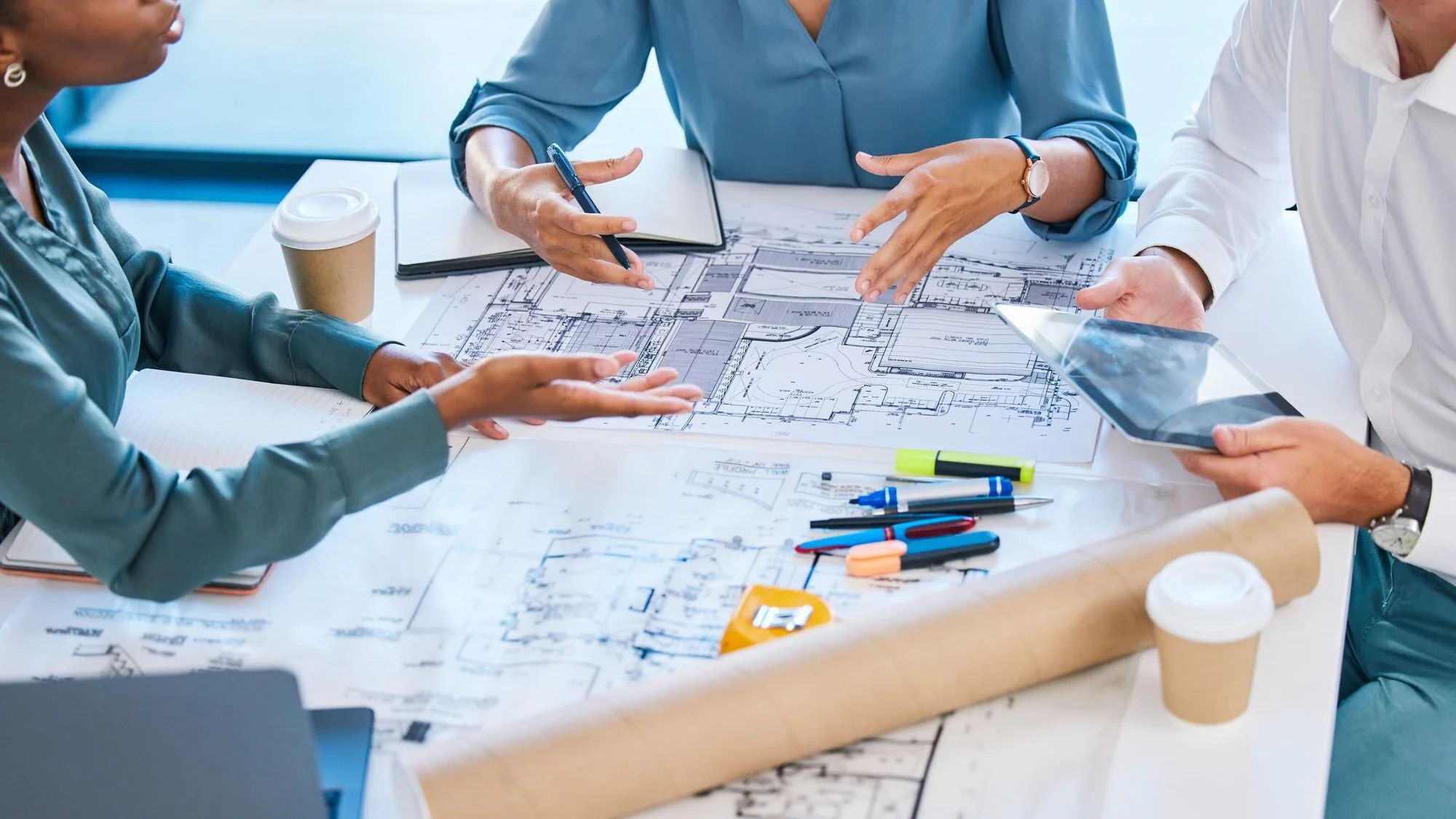 Arkitekter och byggnadsingenjörer samordnar en renovering med ritningar och surfplatta inför val av entreprenadform