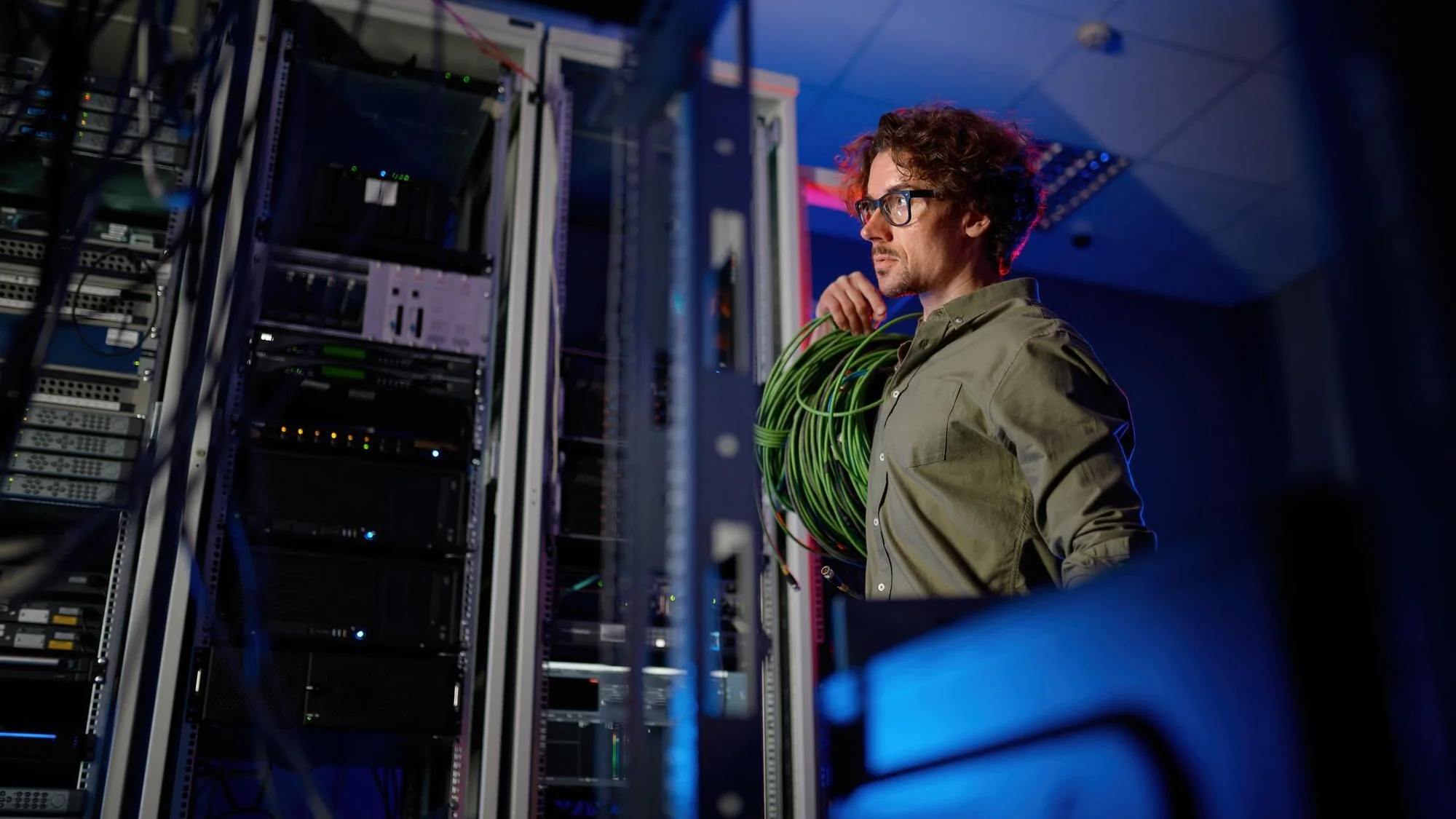Datacenteringenjör går mellan serverrack och fiberoptiska kablar